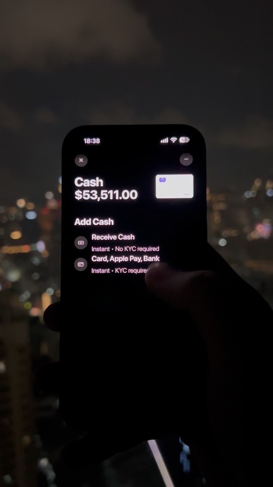 A phone held at night over a lit city, showing the Cash screen at $53,511.00 and its Add Cash options.