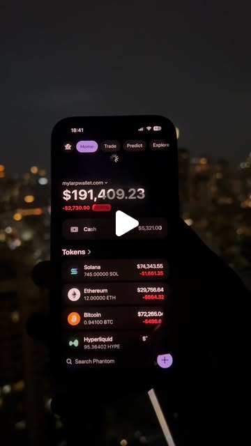 A phone held up at night over city lights, showing a wallet balance of $191,409.23 above its token list.